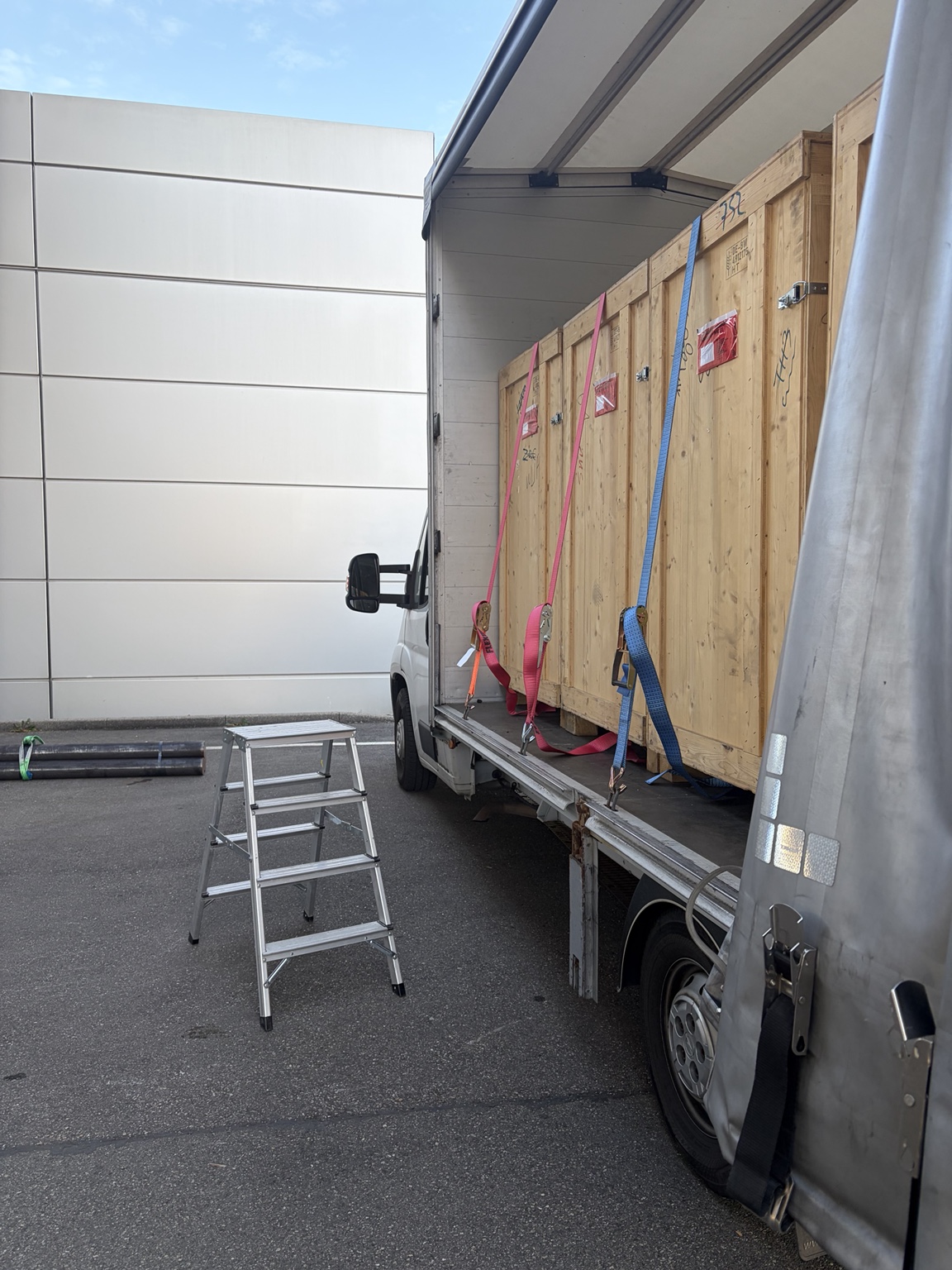 Seitlich geöffneter Planensprinter mit großen Holzkisten und Spanngurten auf der Ladefläche